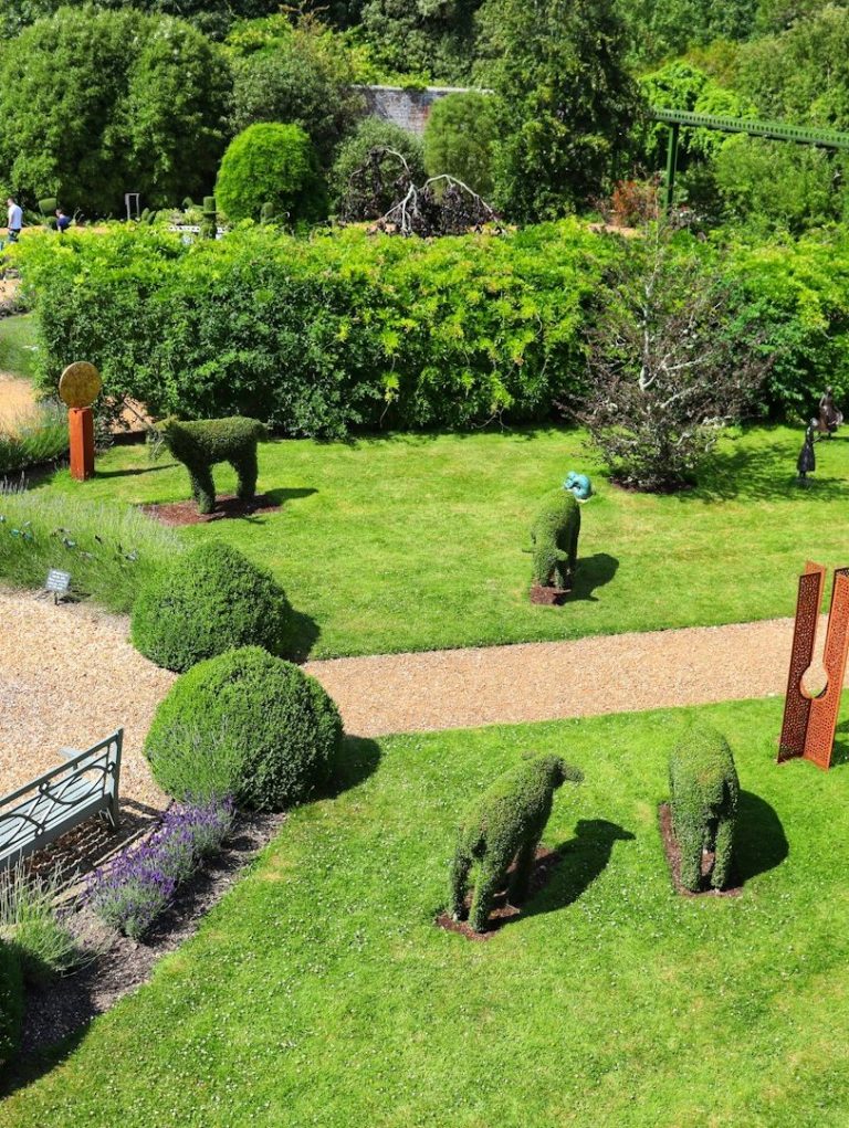Topiaries in Form von Tieren in einem gepflegten Garten mit bunten Pflanzen.